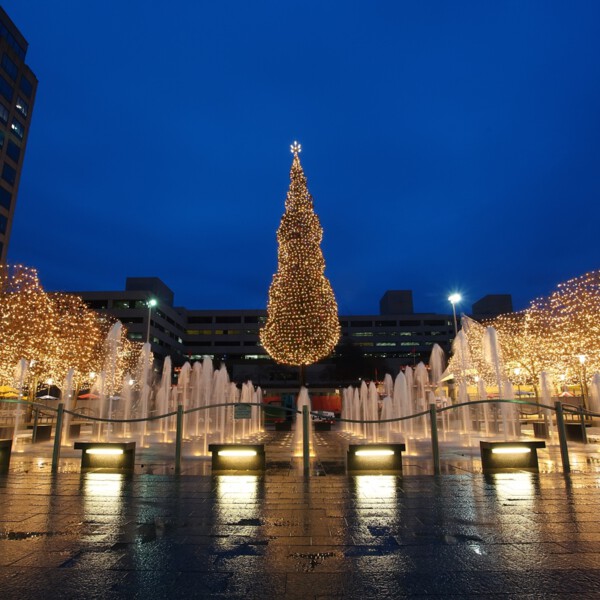Crown Center plaza at night with a large illuminated Christmas tree, light-wrapped trees, and water fountains
